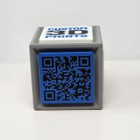 3D printed cube with one side featuring a QR code and the other featuring logos and slogans.